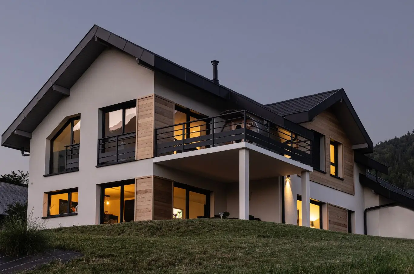 Maison contemporaine avec bardage bois, balcon et bain nordique au crépuscule en Haute-Savoie