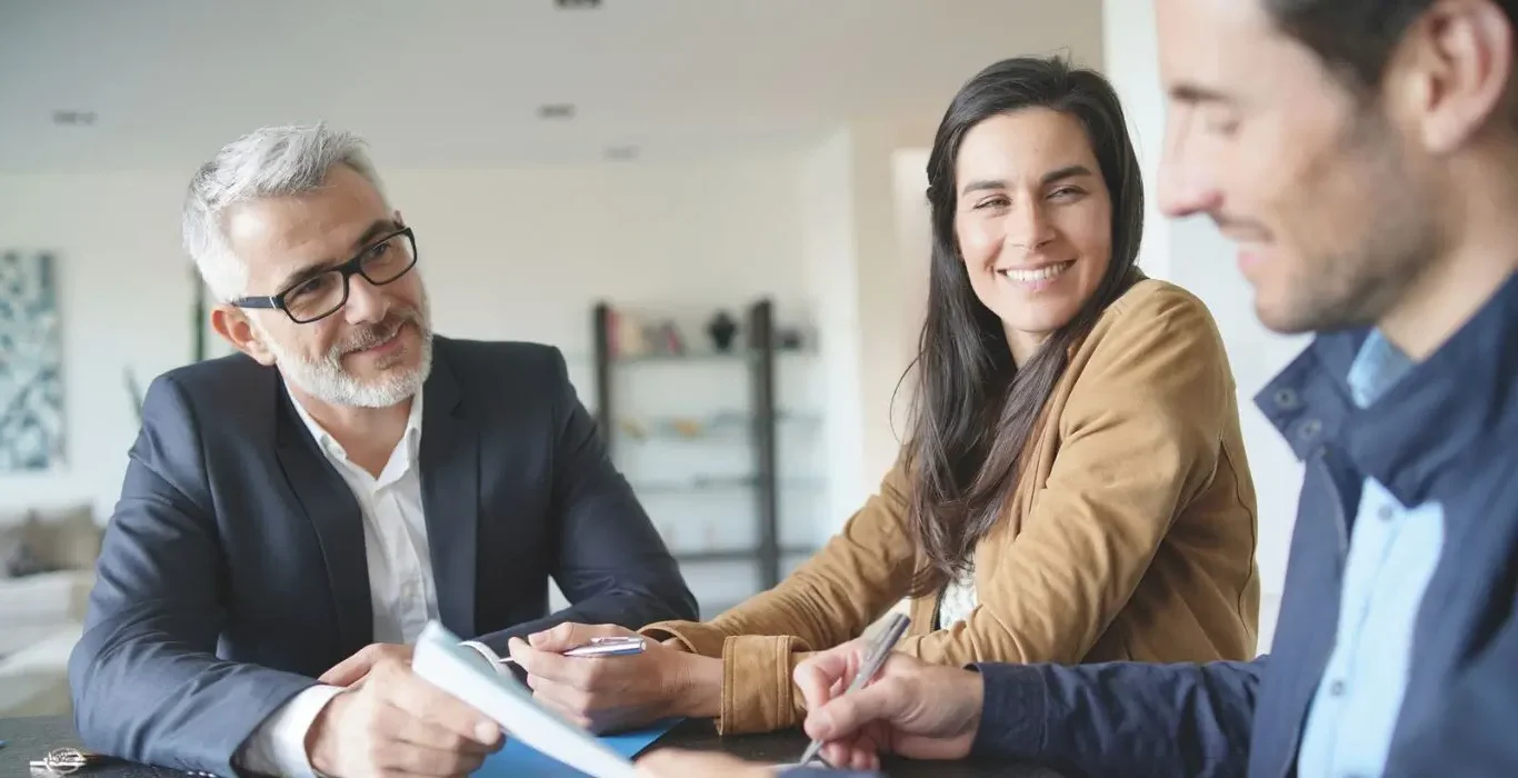 Couple échangeant avec un conseiller immobilier dans un bureau moderne pour un projet de construction de maison en Haute-Savoie.