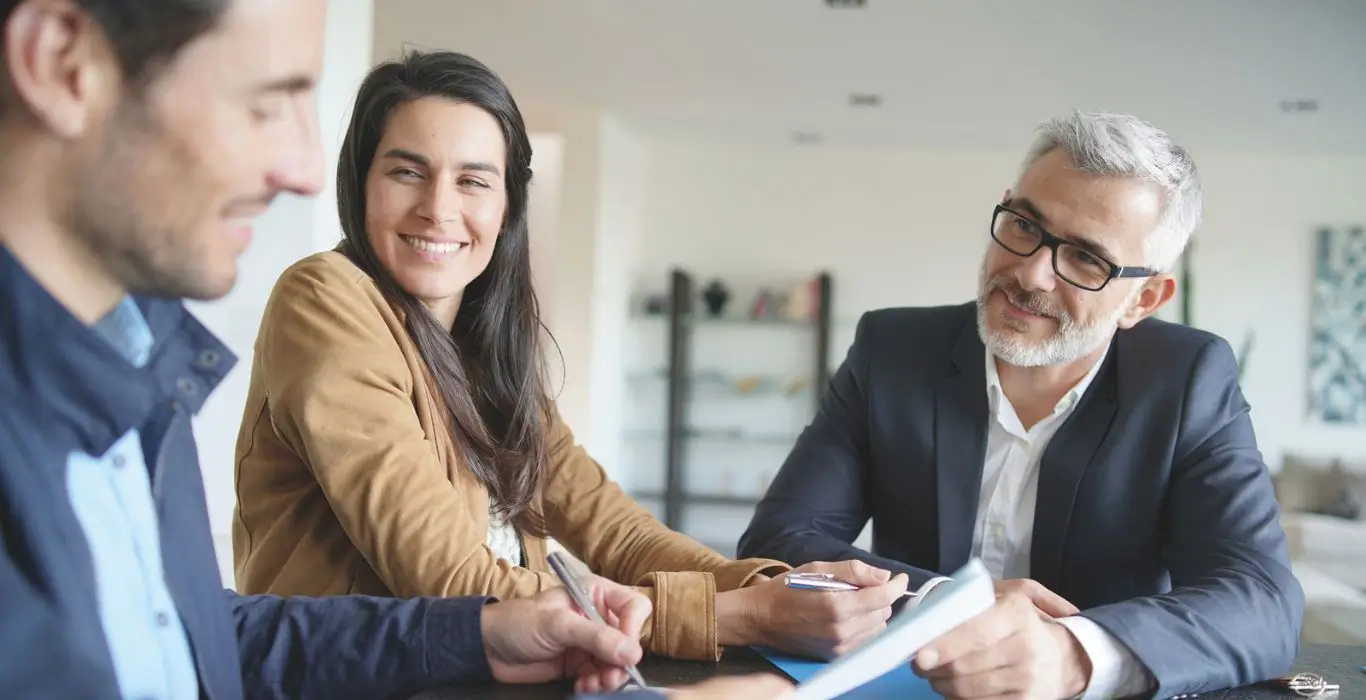 Couple échangeant avec un conseiller immobilier dans un bureau moderne pour un projet de construction de maison en Haute-Savoie.