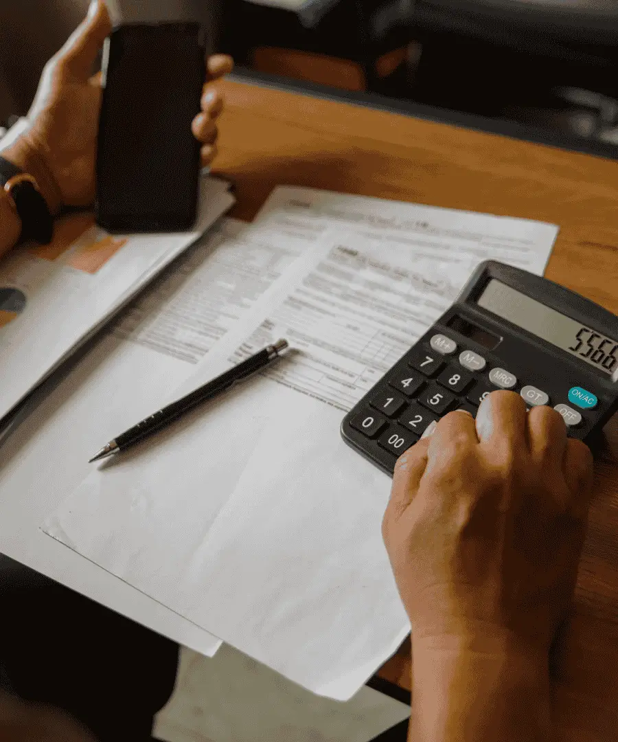 Personne calculant le budget de construction d'une maison avec une calculatrice et des documents financiers