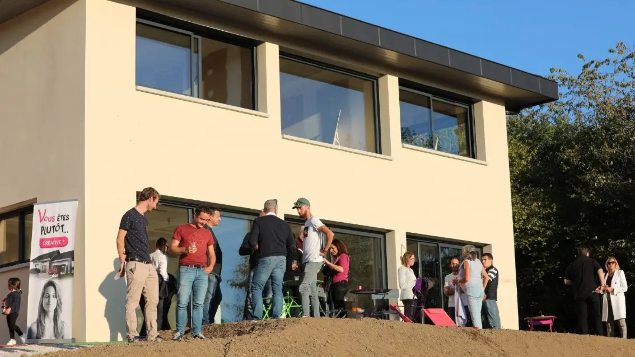 Visiteurs réunis devant une maison contemporaine à l’occasion d’une porte ouverte au coucher du soleil.