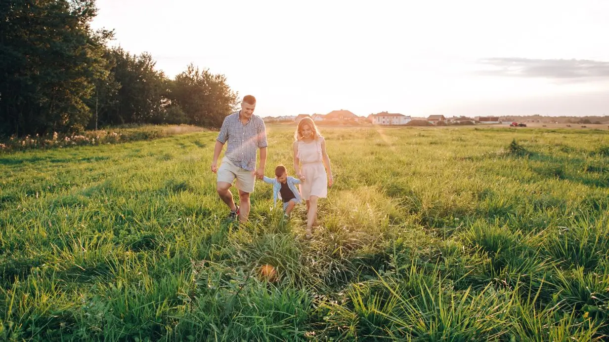 Jeune famille explorant un terrain ensoleillé pour construire leur future maison individuelle en Haute-Savoie.