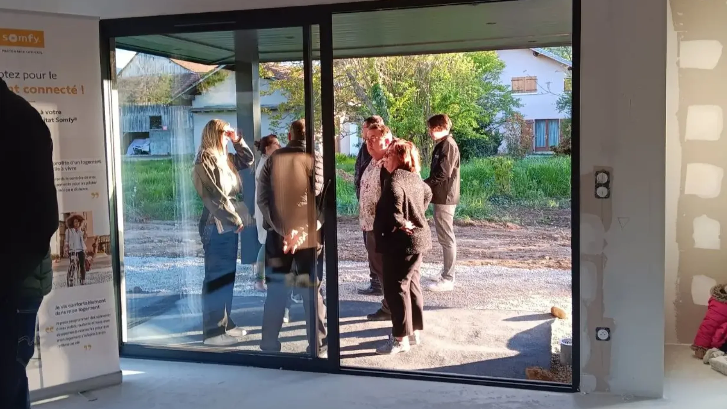 Petit groupe discutant à travers la baie vitrée d’un logement moderne en construction.