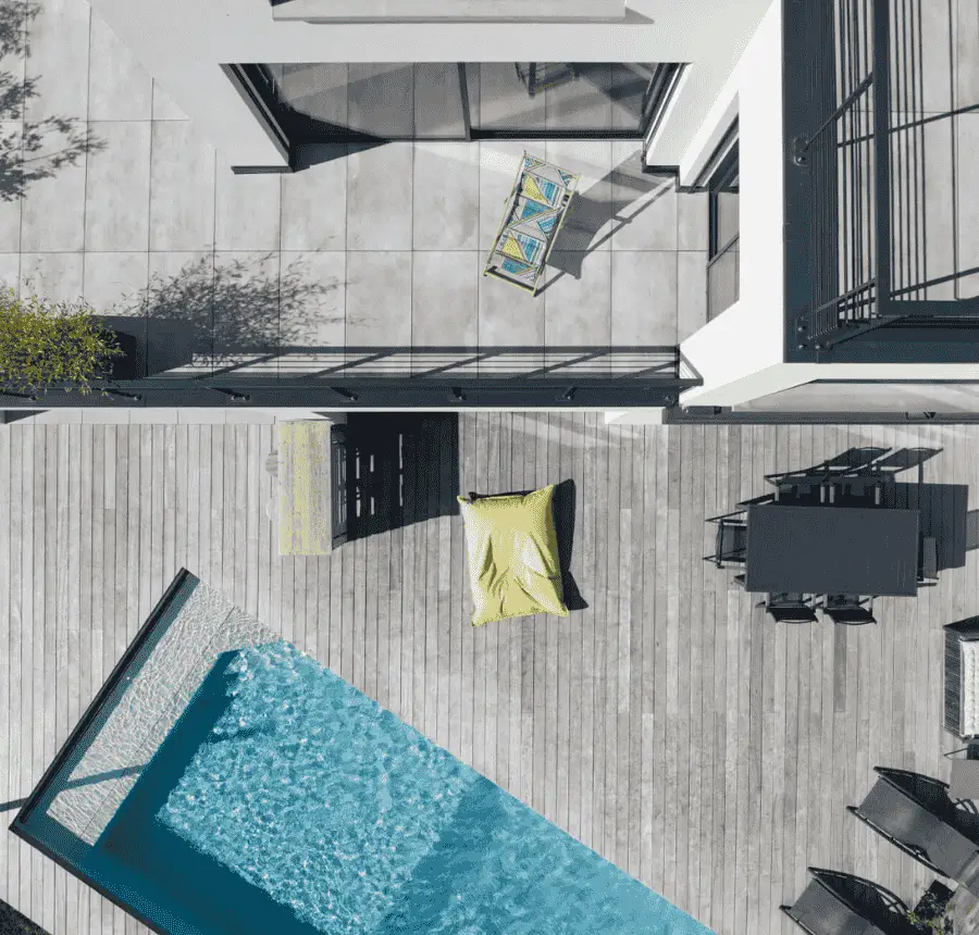 Vue aérienne d’une terrasse en bois avec piscine carrée, transats et mobilier de jardin.