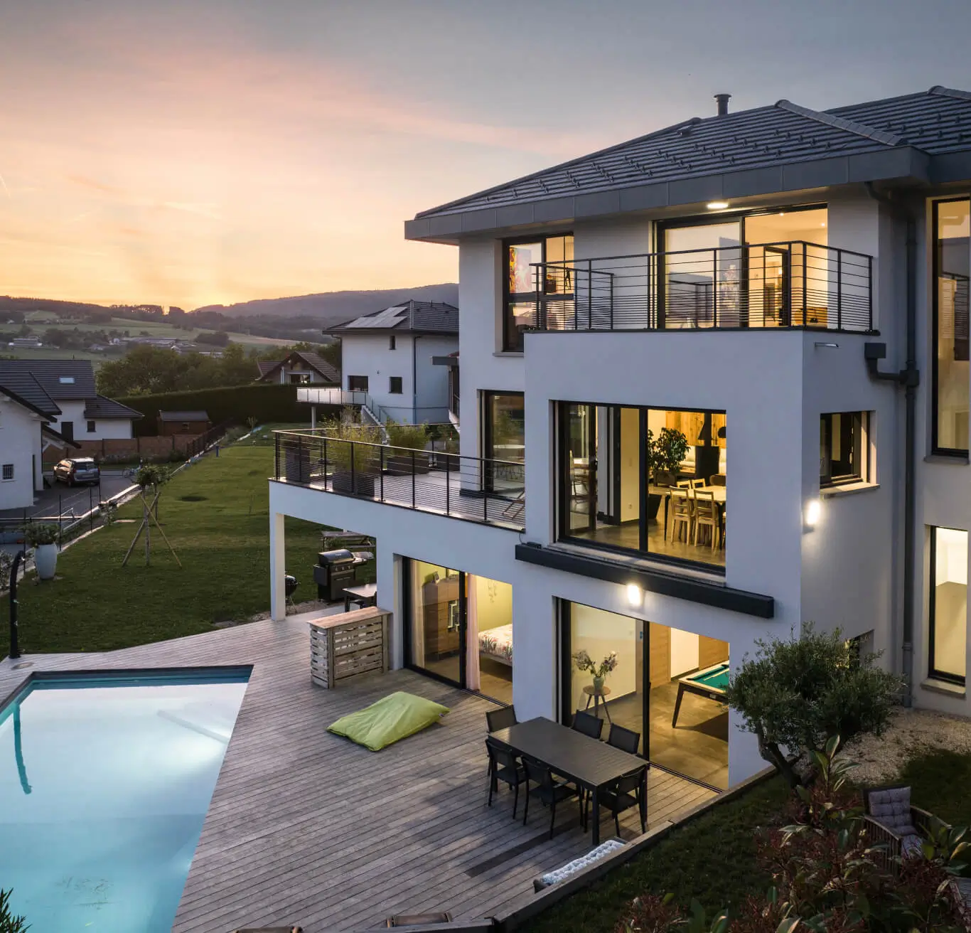 Maison contemporaine à Groisy avec terrasse bois, piscine et grandes ouvertures vitrées au crépuscule