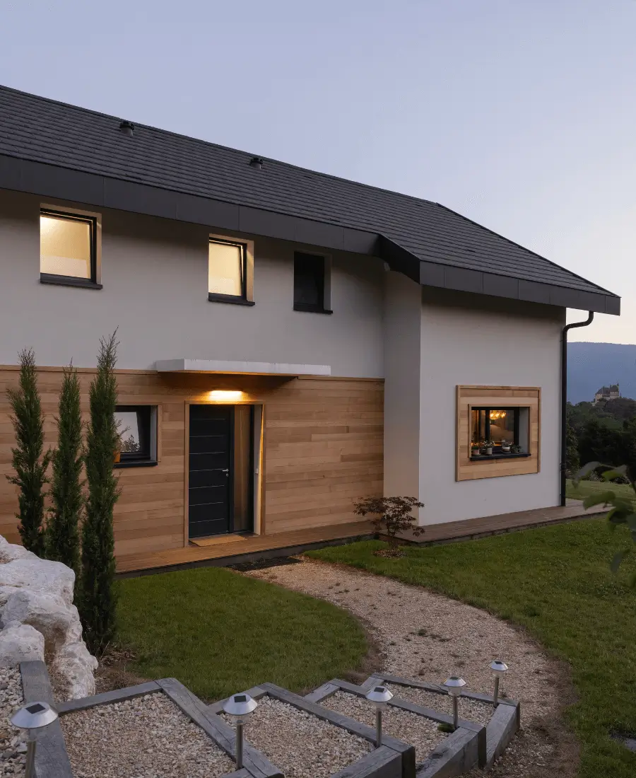 Maison moderne à Bluffy en Haute-Savoie avec façade en bois et entrée illuminée au crépuscule
