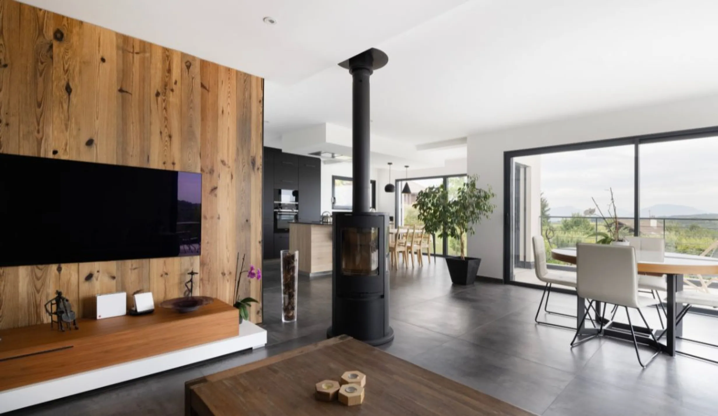 Espace de vie moderne et chaleureux avec poêle à bois, grandes baies vitrées et vue dégagée.