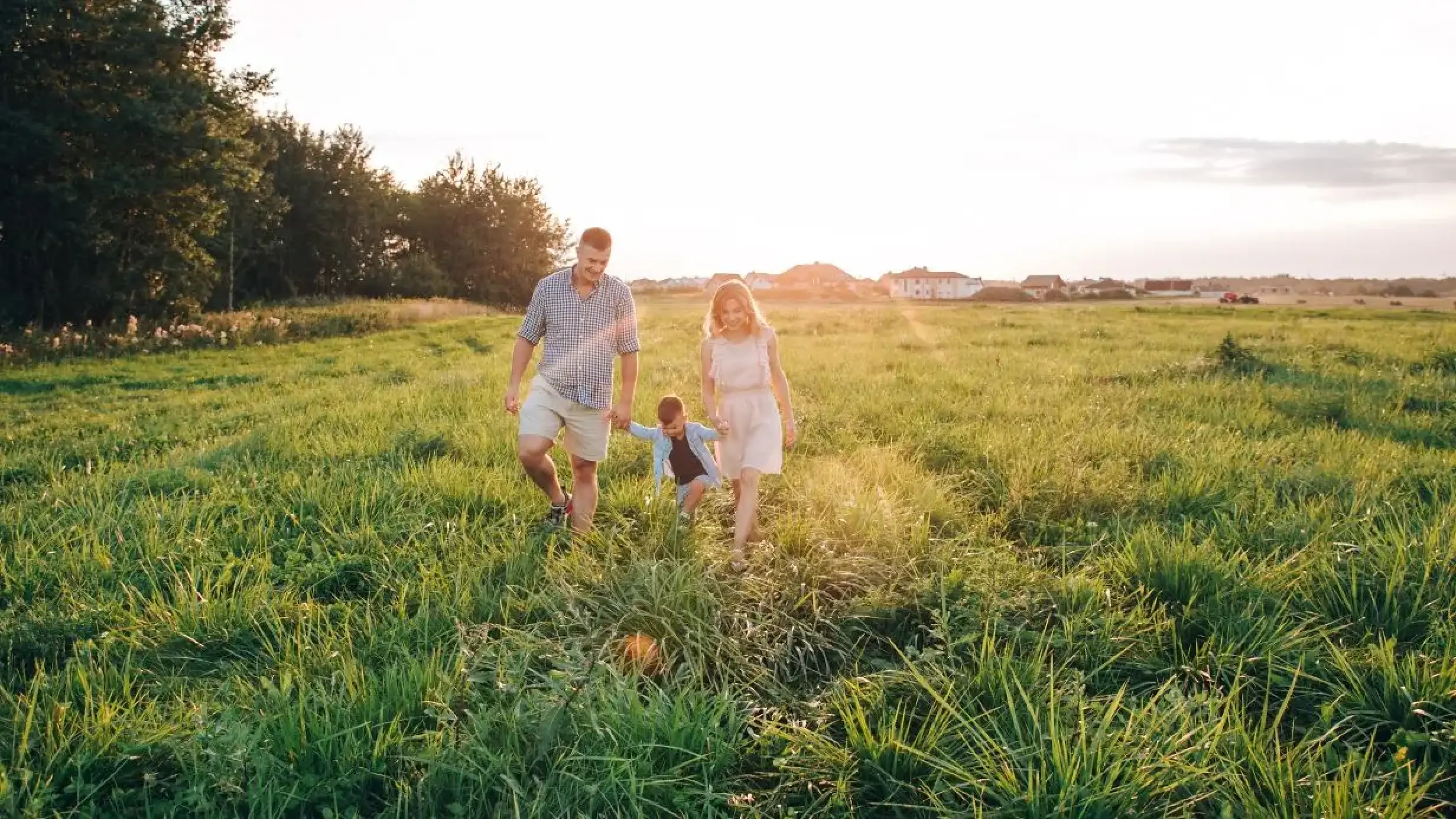 Jeune famille explorant un terrain ensoleillé pour construire leur future maison individuelle en Haute-Savoie.