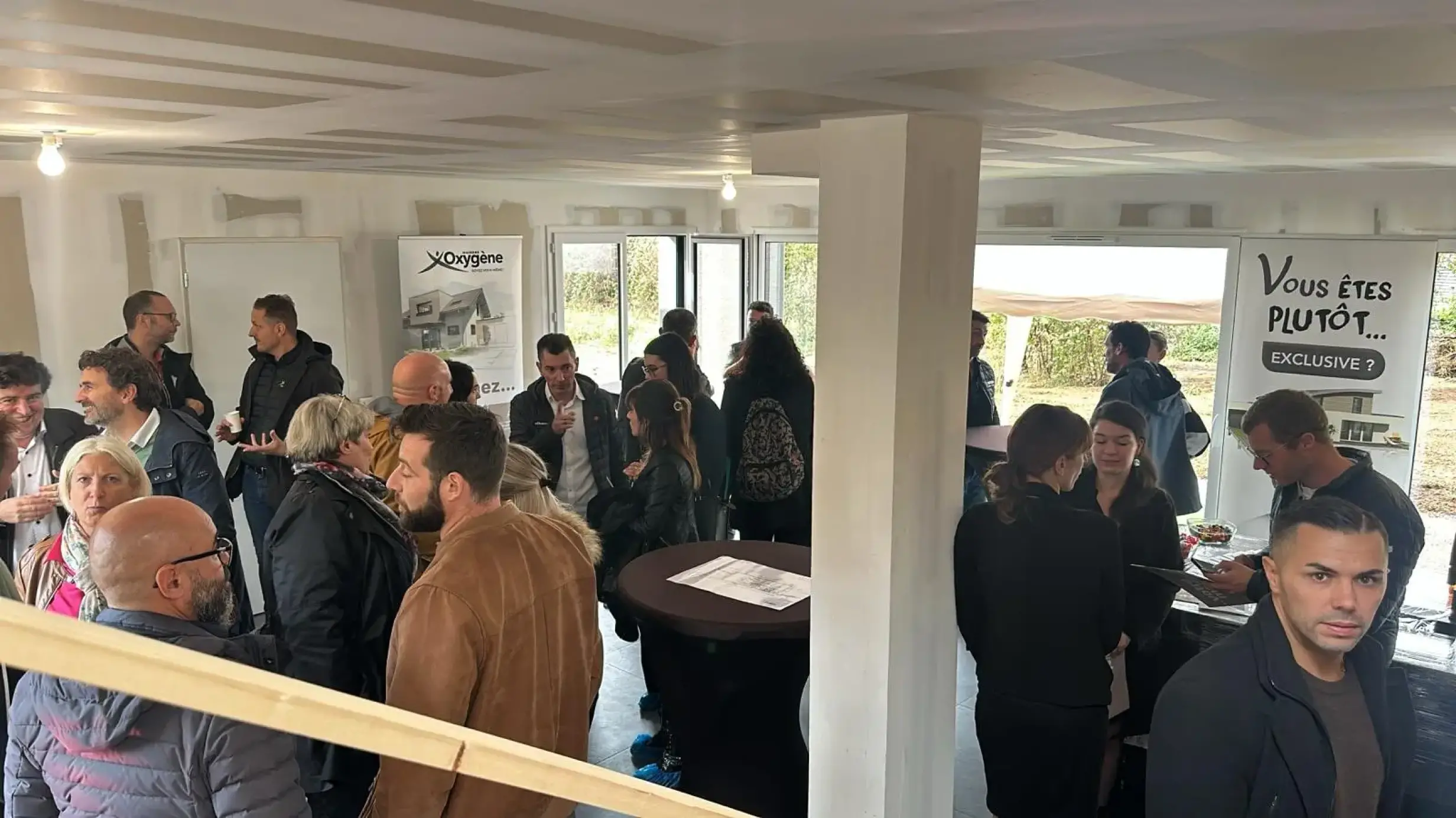 De nombreux visiteurs participent à un échange collectif lors d’une porte ouverte dans un intérieur en finition.