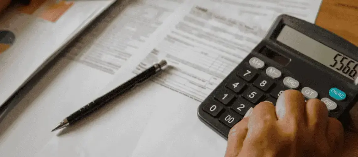 Personne calculant le budget de construction d'une maison avec une calculatrice et des documents financiers