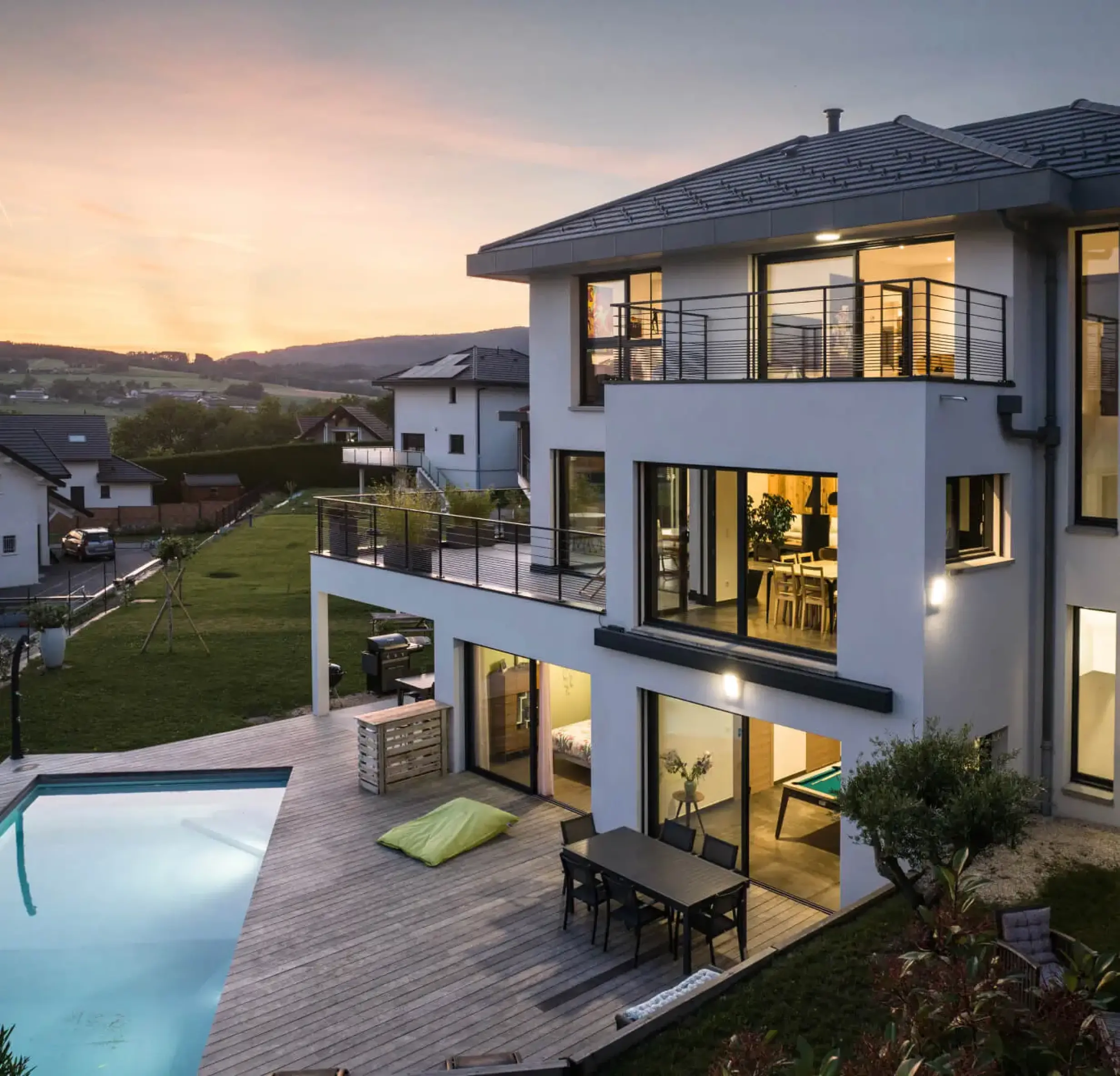 Maison contemporaine à Groisy avec terrasse bois, piscine et grandes ouvertures vitrées au crépuscule